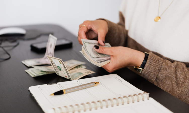 A woman sitting at a desk with a notebook open and counting money